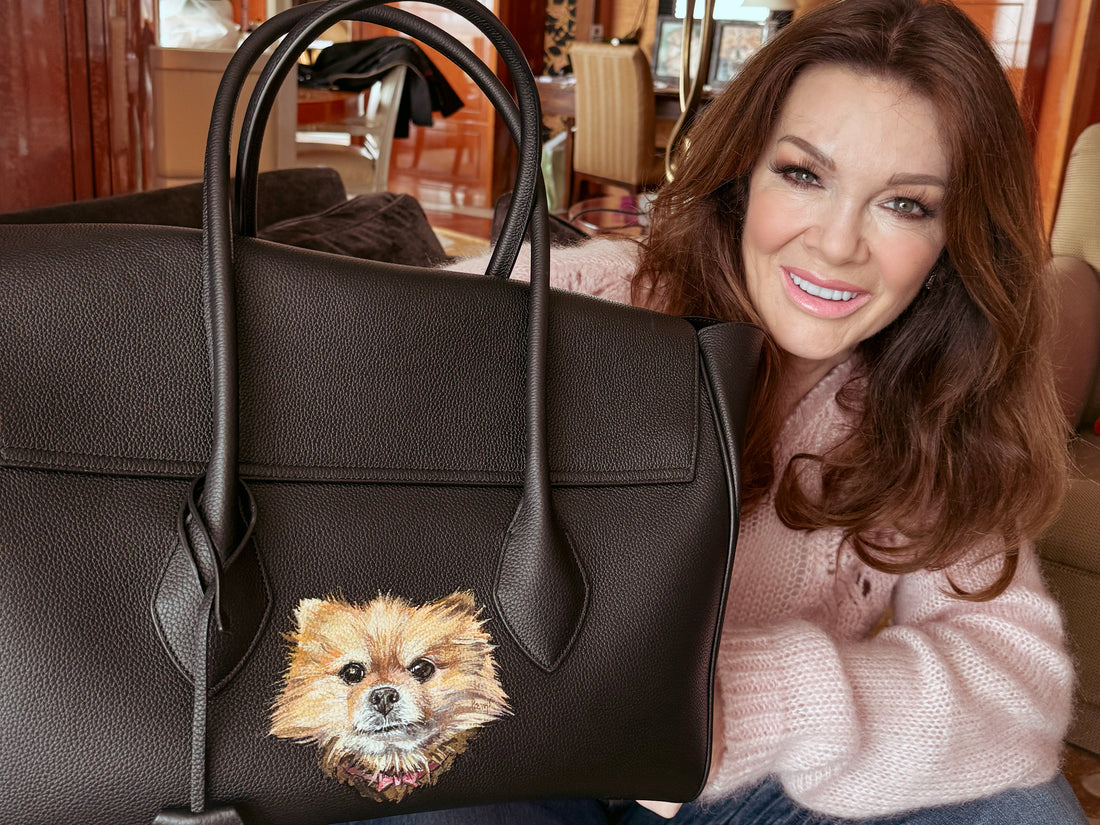 Lisa Vanderpump holding a bespoke Ferragamo handbag featuring hand-painted portraits of her beloved dogs by luxury pet portrait artist Aivis Provejs.
