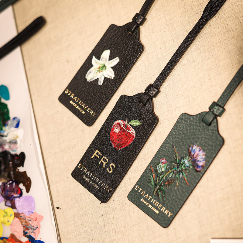 Hand-painted Strathberry luggage tags featuring bespoke botanical artwork, personalised initials and luxury leather customisation by Aivis Provejs.
