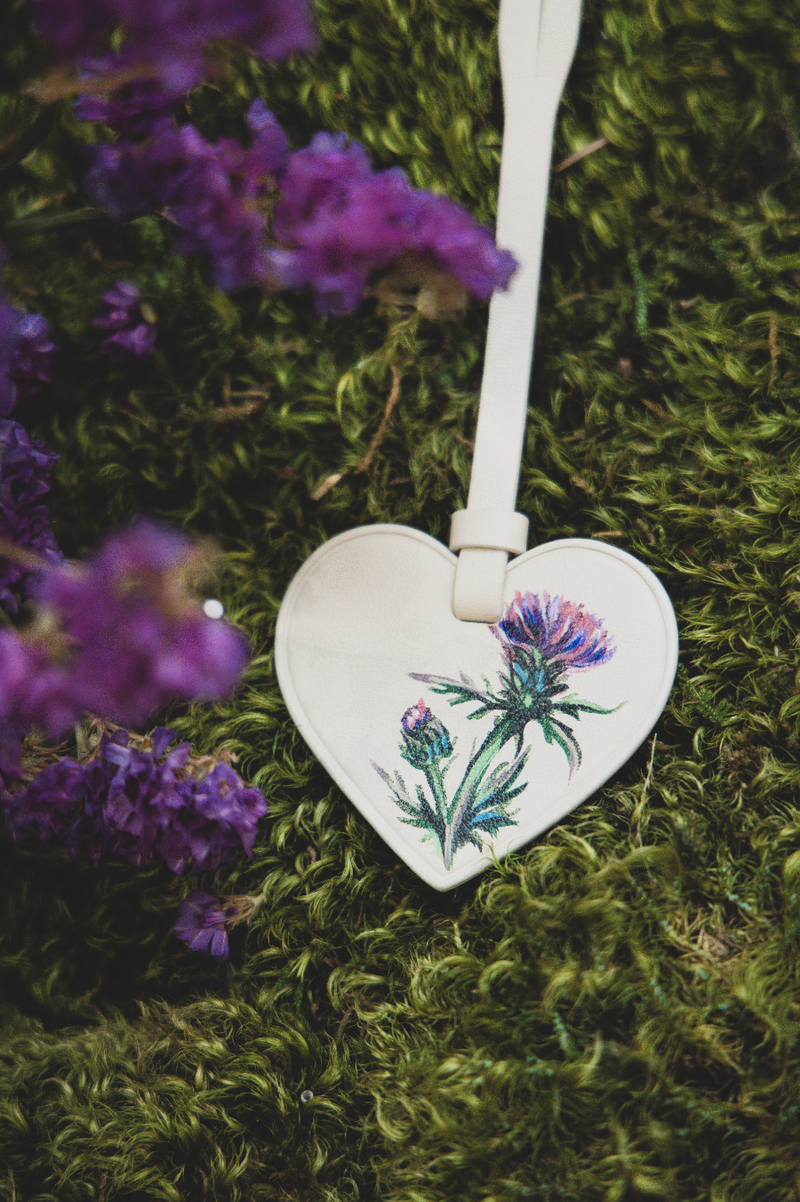 Hand-painted Scottish thistle illustration on a Strathberry heart-shaped leather luggage tag by Aivis Provejs, bespoke luxury leather personalisation.